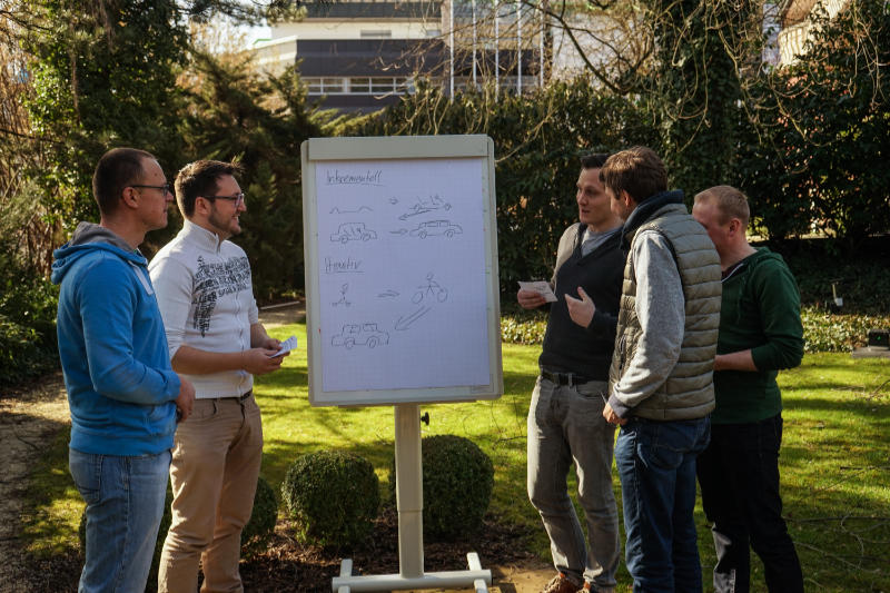Schulungsteilnehmer stehen im Garten und diskutieren Agile Softwareentwicklung auf einem Flip Chart